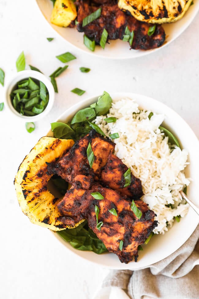 Grilled pineapple chicken served in a bowl with greens and white rice. 