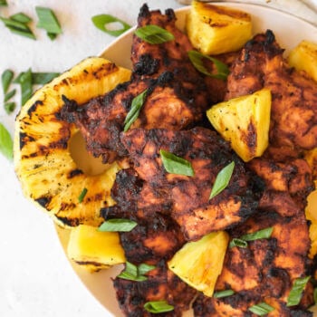 Grilled pineapple chicken on a plate with sliced green onions on top