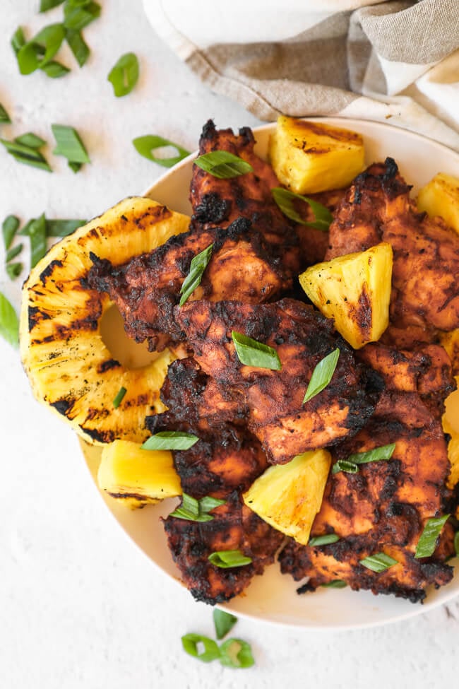 Grilled pineapple chicken on a plate with sliced green onions on thp