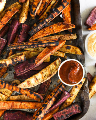 Vertical overhead image of grilled sweet potato fries on a grilling pan with ketchup and chipotle aioli on the side.