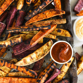 Vertical overhead image of grilled sweet potato fries on a grilling pan with ketchup and chipotle aioli on the side.