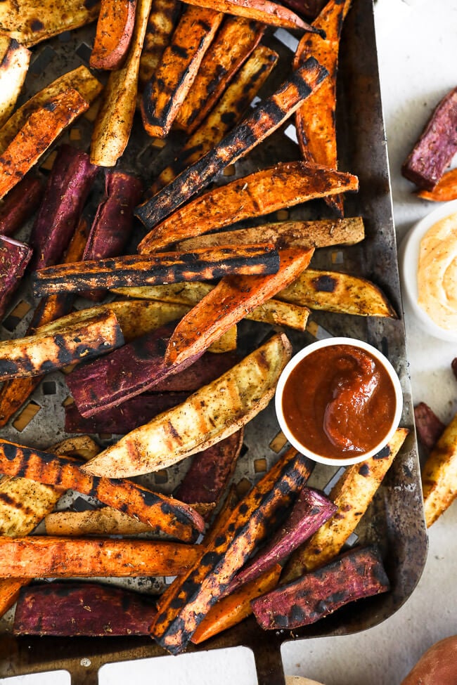 Vertical overhead image of grilled sweet potato fries on a grilling pan with ketchup and chipotle aioli on the side.