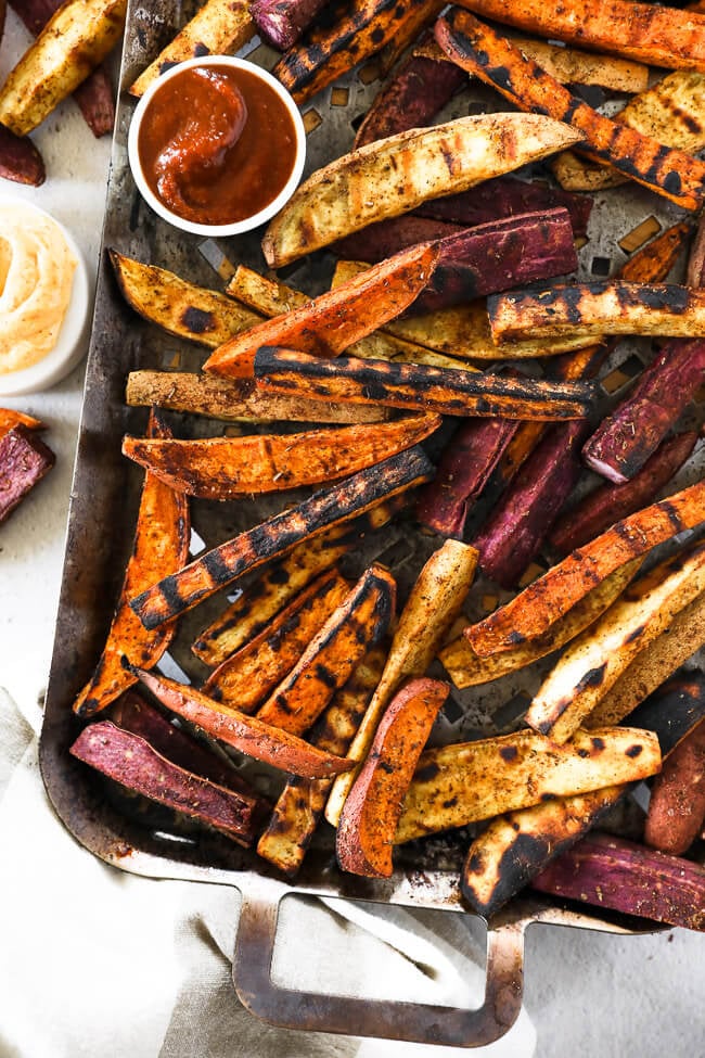 Vertical overhead image of grilled sweet potato fries on a grilling pan with ketchup and chipotle aioli on the side. 
