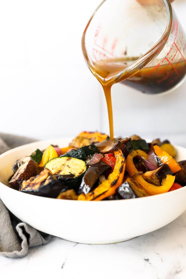Image of pouring vegetable marinade over a bowl full of grilled vegetables. 