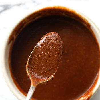 Close up overhead image of spoonful of homemade BBQ sauce over a ramekin full of sauce