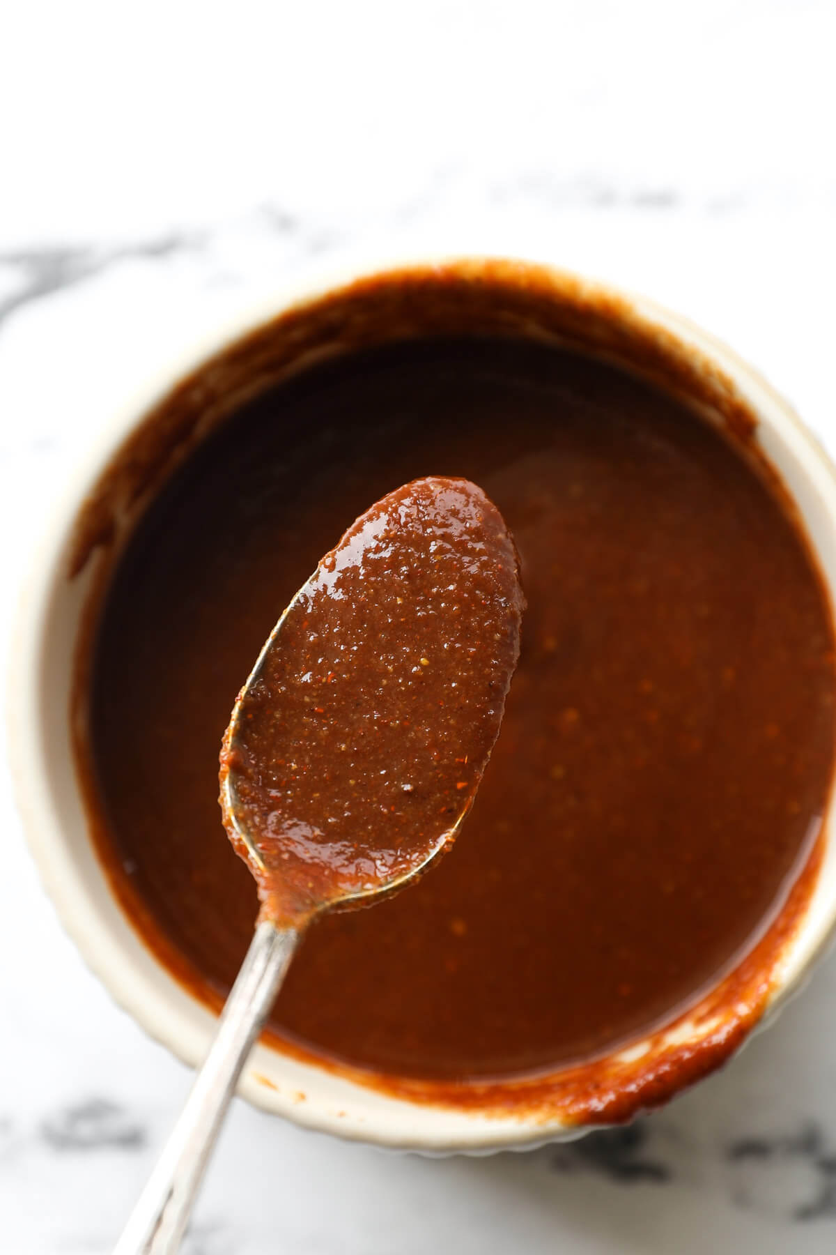 Close up overhead image of spoonful of homemade BBQ sauce over a ramekin full of sauce