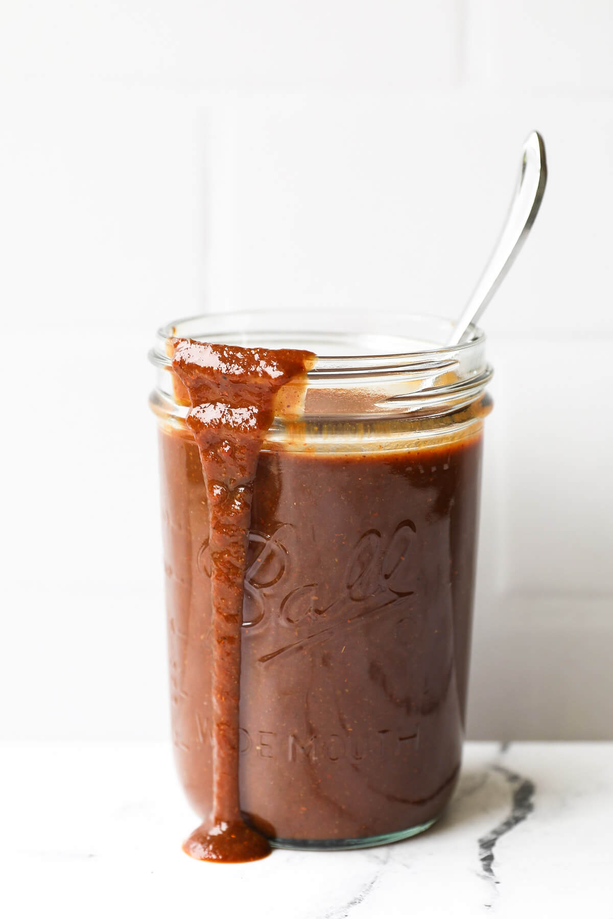 Healthy homemade whole30 BBQ sauce in a jar with spoon and sauce running down front of jar
