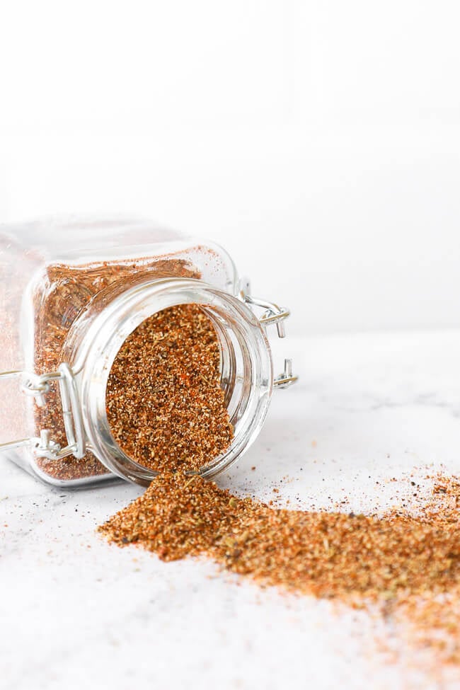 Homemade taco seasoning in a jar tipped over on side with seasoning spilling out