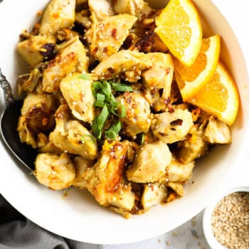 Chunks of orange chicken in a bowl with orange wedges