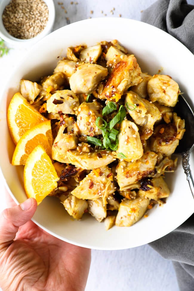 Healthy instant pot orange chicken in a bowl with orange wedges and hand holding bowl 