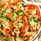 Marinated chicken stir fry with broccoli, onion and bell pepper in a skillet with spoon