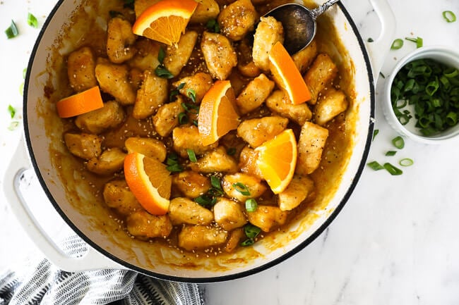 Healthy orange chicken in pan with orange slices and spoon horizontal image.