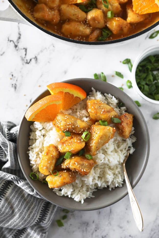 Healthy orange chicken in a bowl over rice with spoon overhead vertical image