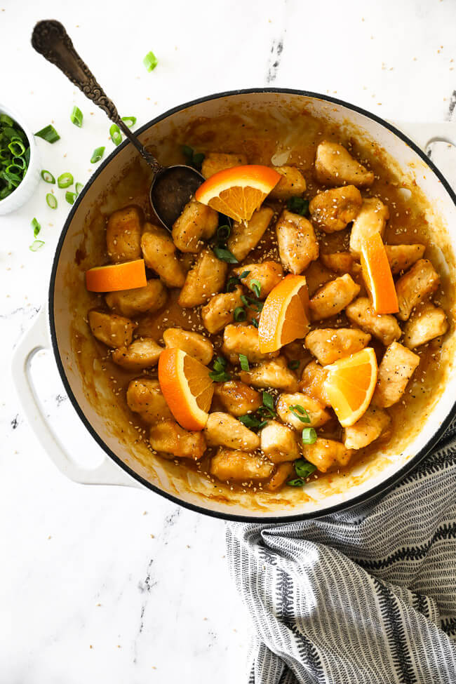 Healthy orange chicken in pan with orange slices and spoon vertical image.