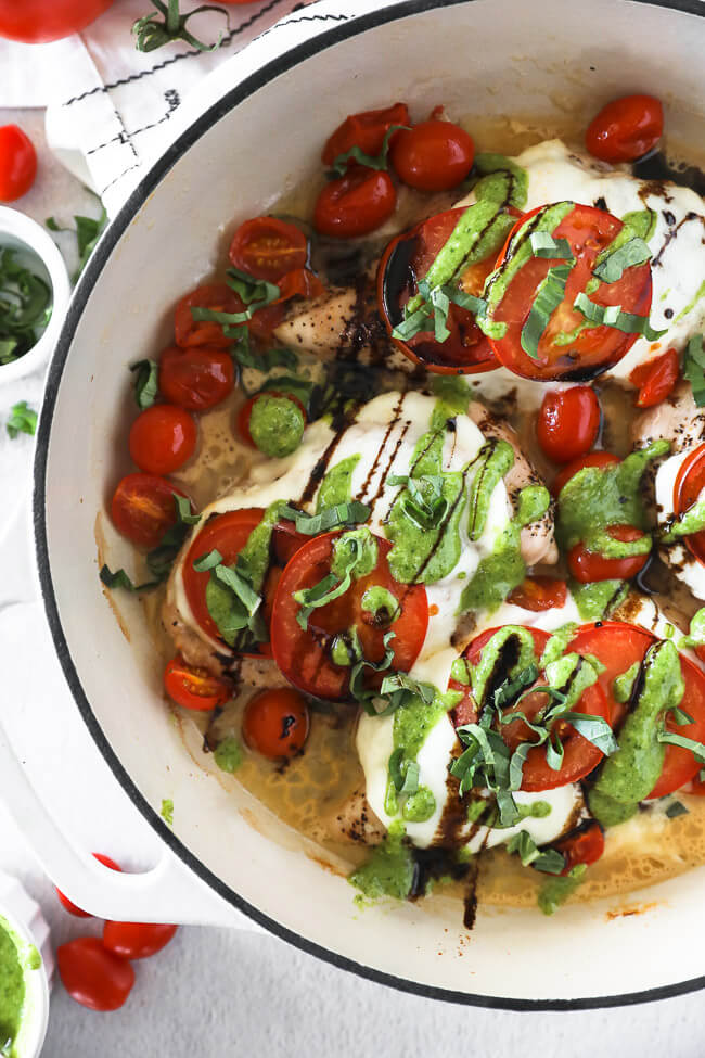 Vertical overhead image of chicken caprese in skillet. Chicken breasts topped with mozzarella cheese, tomatoes, pesto, balsamic and fresh basil. 