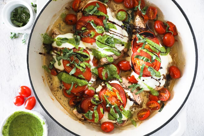 Horizontal overhead image of chicken caprese in skillet. Chicken breasts topped with mozzarella cheese, tomatoes, pesto, balsamic and fresh basil. 