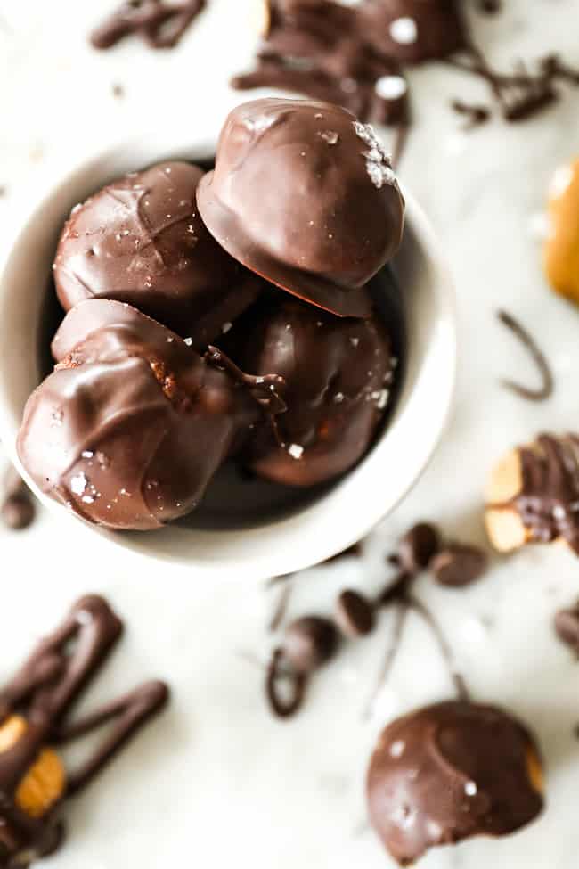 Chocolate coated peanut butter balls with flaky sea salt on top in a small bowl. 