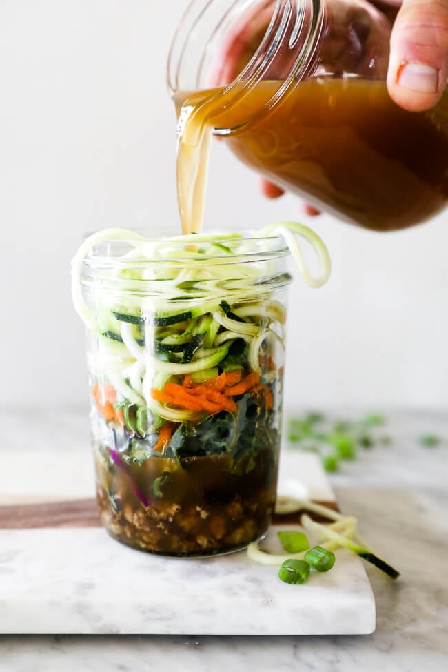 Straight on vertical image of pouring broth into healthy ramen noodles in a jar. 