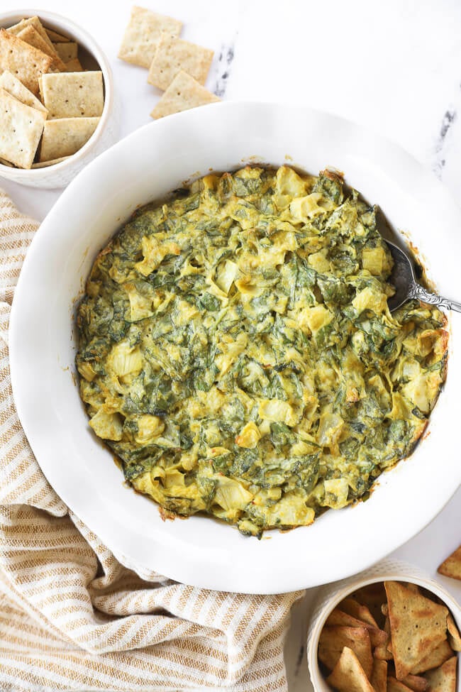 Overhead image of spinach artichoke dip in a serving dish with a spoon dug in. 