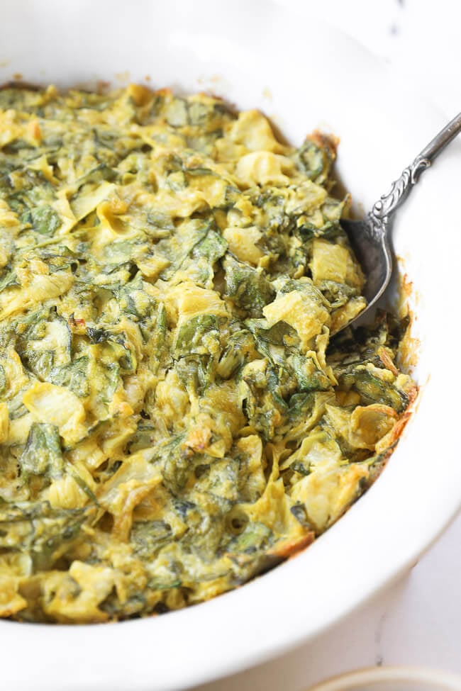 Angled image of spinach artichoke dip in a serving dish with a spoon dug in. 