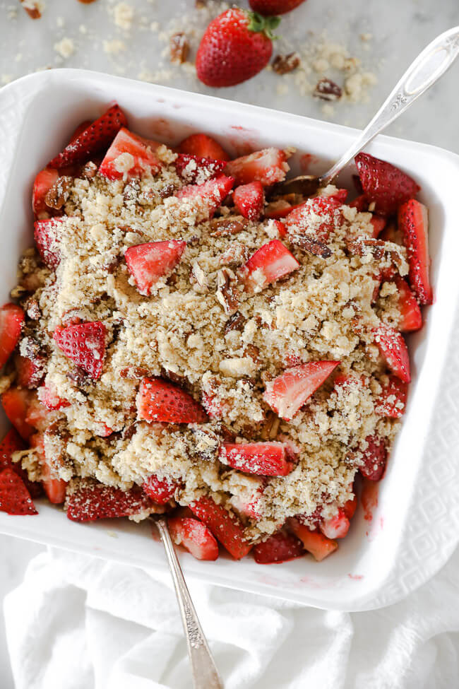 Vertical overhead image of baked strawberry crumble in baking dish with two spoons dug in. 