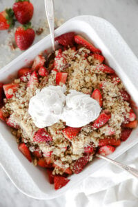 Fresh strawberry crumble in a dish with two scoops of vanilla ice cream on top