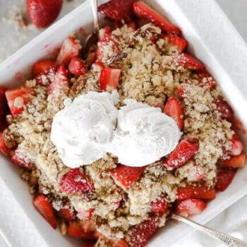 Fresh strawberry crumble in a dish with two scoops of vanilla ice cream on top