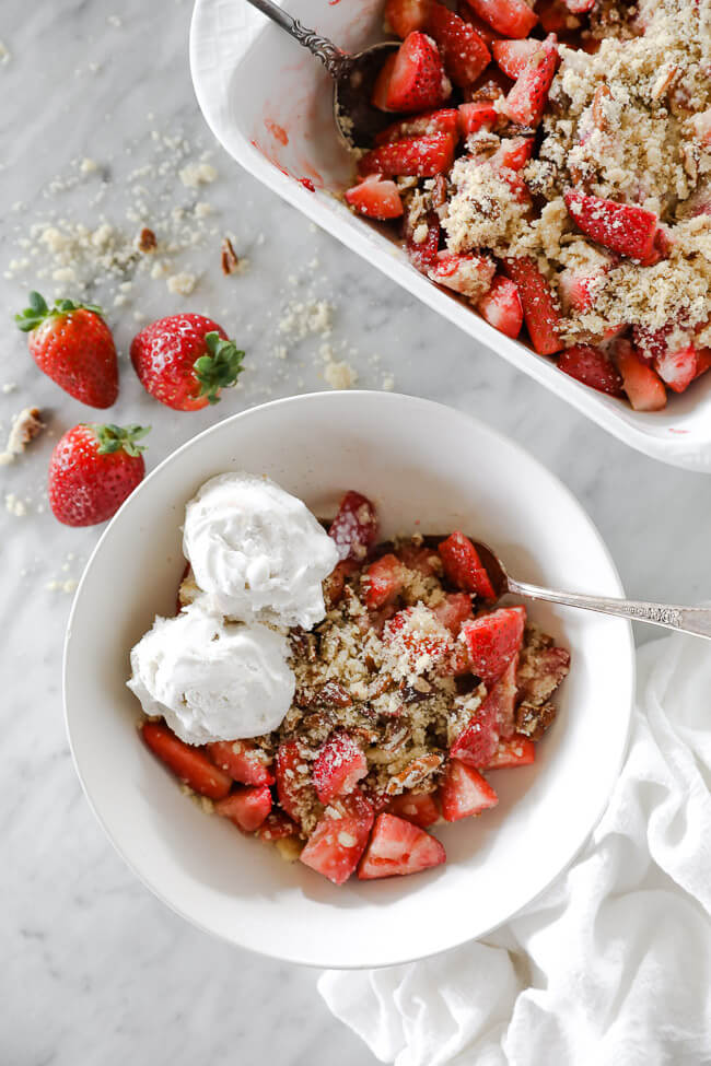 Vertical overhead image of strawberry crumble served up in a bowl with dairy-free ice cream on top and a spoon dug in. 