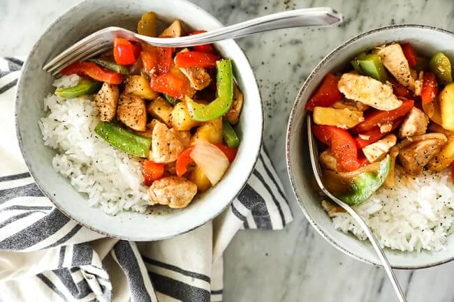 Overhead shot of healthy sweet and sour chicken served up in two bowls with white rice and forks dug into bowls. 