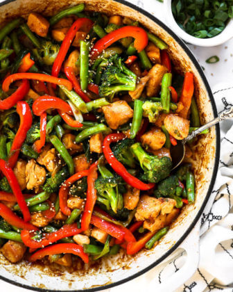 Close up overhead image of healthy teriyaki chicken in a skillet with a serving spoon scooped in.