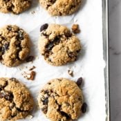 Overhead close up image of six vegan oatmeal raisin cookies on a baking sheet.