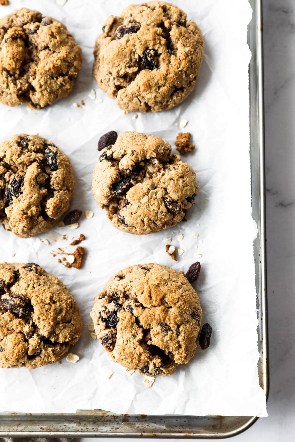 Overhead close up image of six vegan oatmeal raisin cookies on a baking sheet.