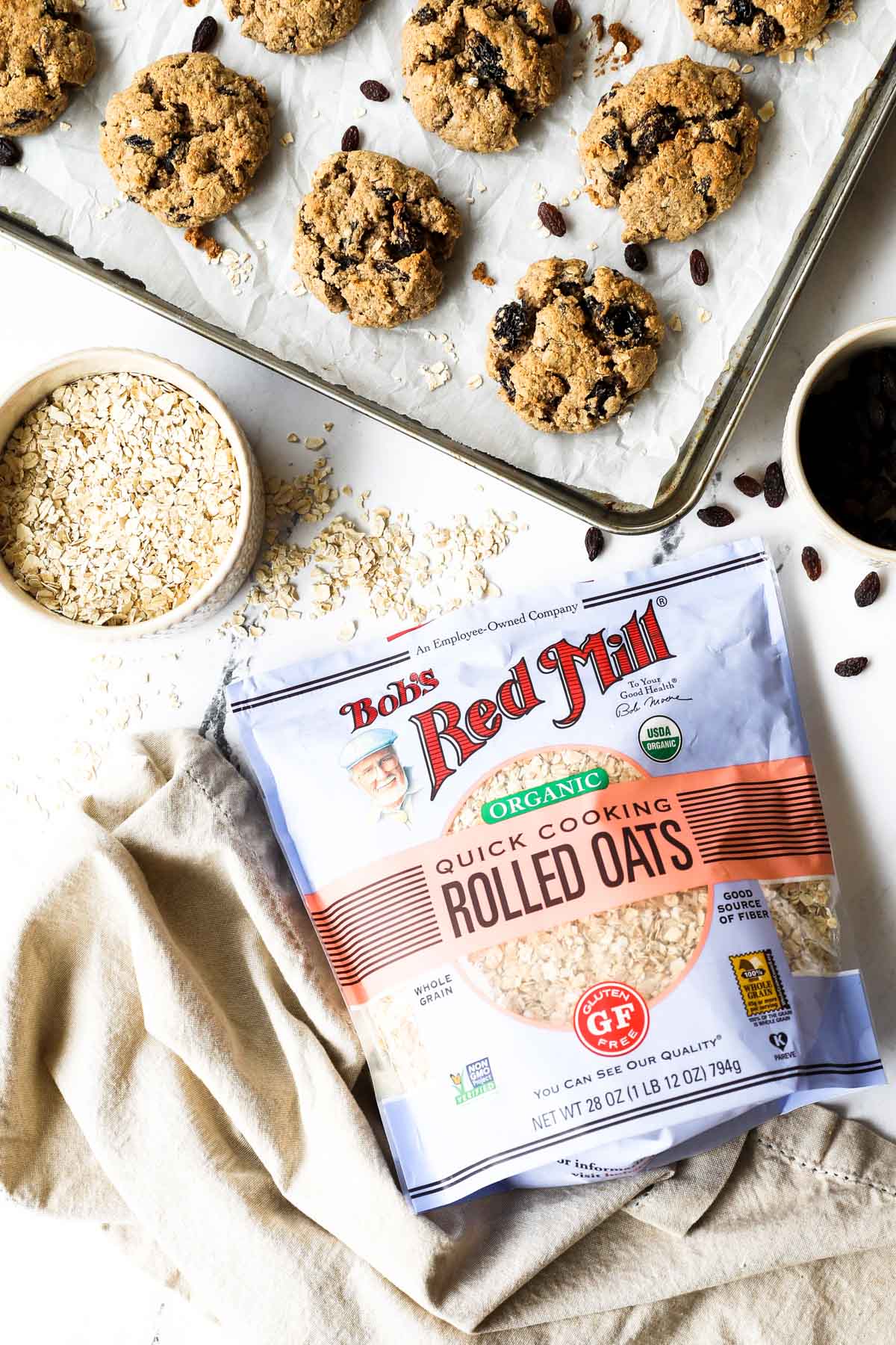 Image of rolled oats and a cookie sheet with oatmeal raisin cookies in the background.