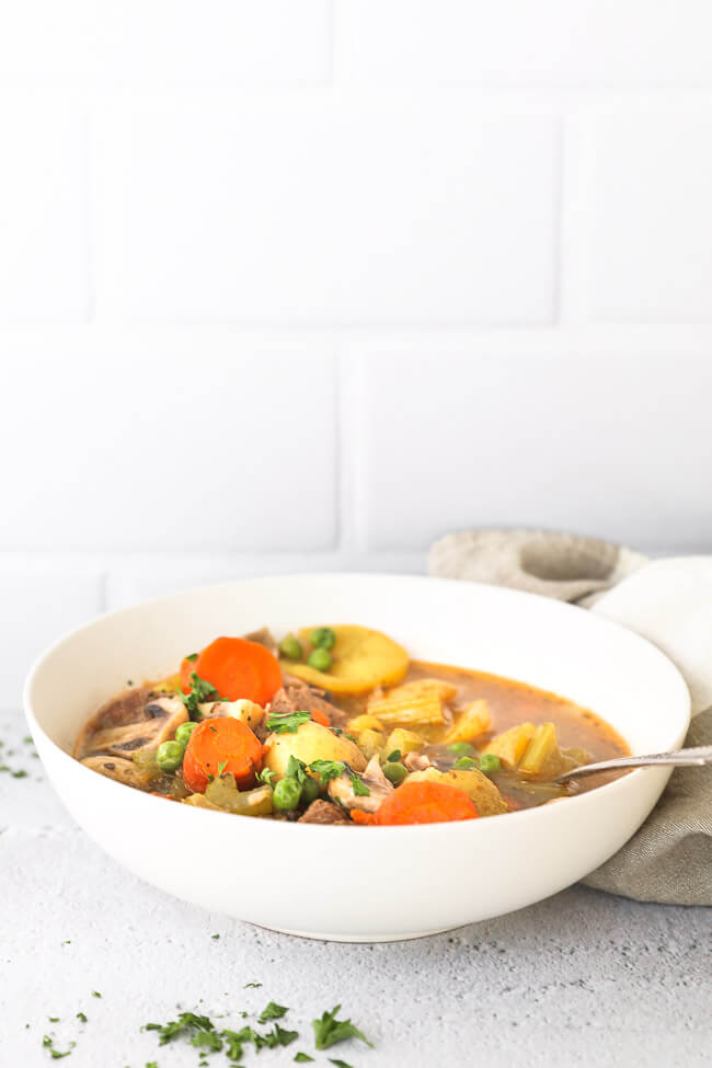 Straight on shot of bowl filled with soup of beef, carrots celery, mushrooms and peas