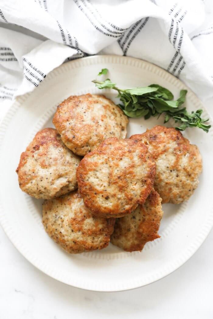 Chicken sausage patties on a plate with some fresh herbs on the plate.