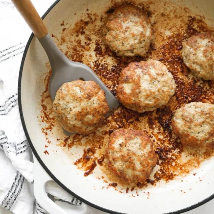 Overhead image of a cast iron skillet with chicken sausage patties in it. A spatula lifting one patty out of the pan.