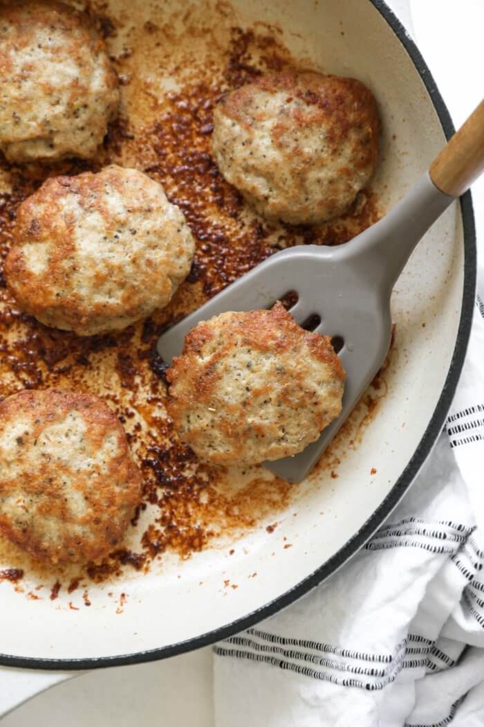 Close up overhead image of skillet with one sausage patty being lifted by a spatula.