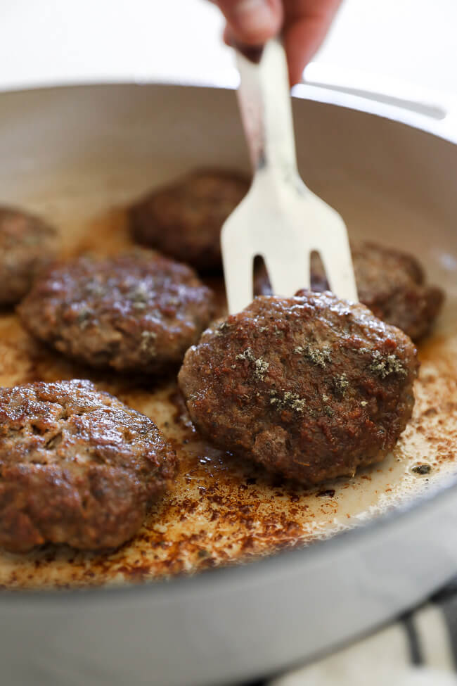 Lifting one homemade country breakfast sausage patty from the skillet with a spatula. 