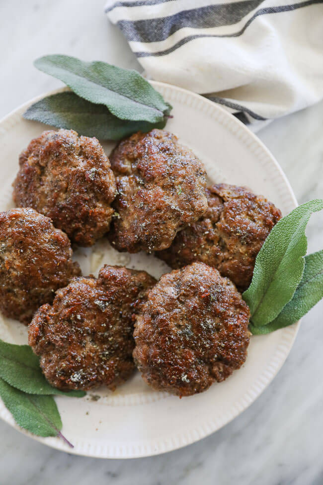 Overhead image of homemade country breakfast sausage patties on a plate with sage leaves. 