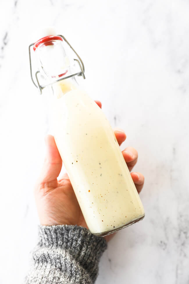 Image of holding a glass dressing jar filled with homemade caesar salad dressing.