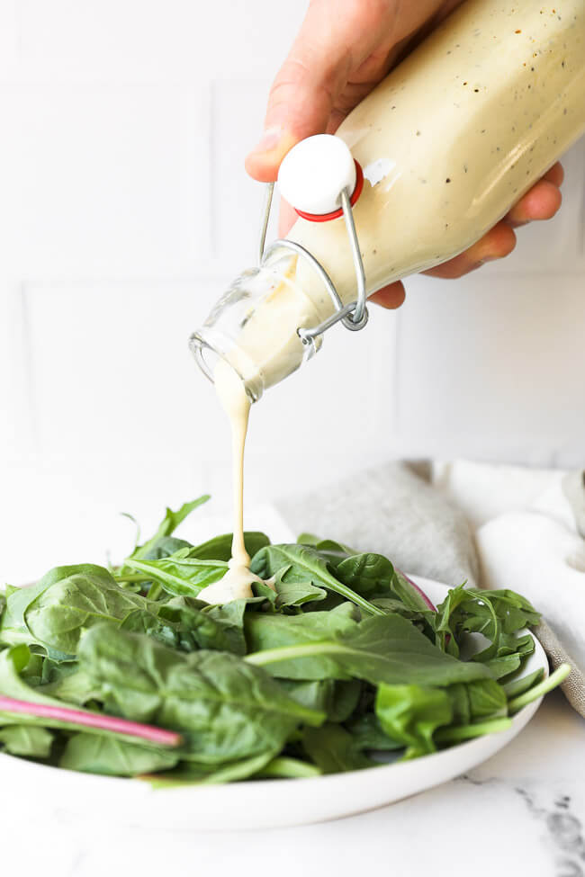 Image of pouring keto caesar dressing onto a plate of greens. 