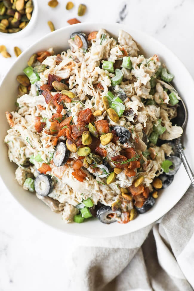 Vertical overhead image of chicken salad in a bowl with a spoon in it and extra bacon on the side. 