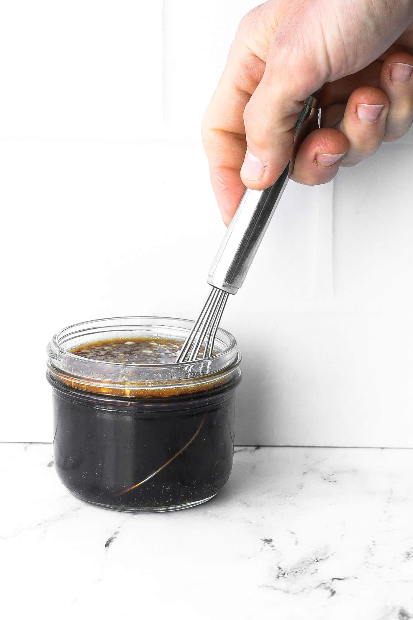 Stirring honey garlic marinade in a small jar with a whisk.