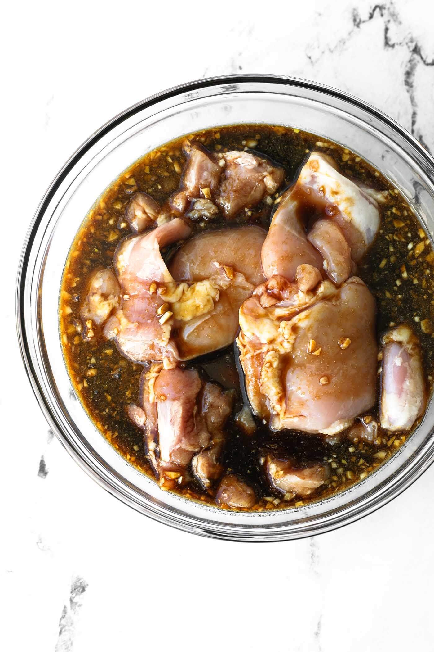 Raw chicken marinating in a bowl with honey garlic sauce.