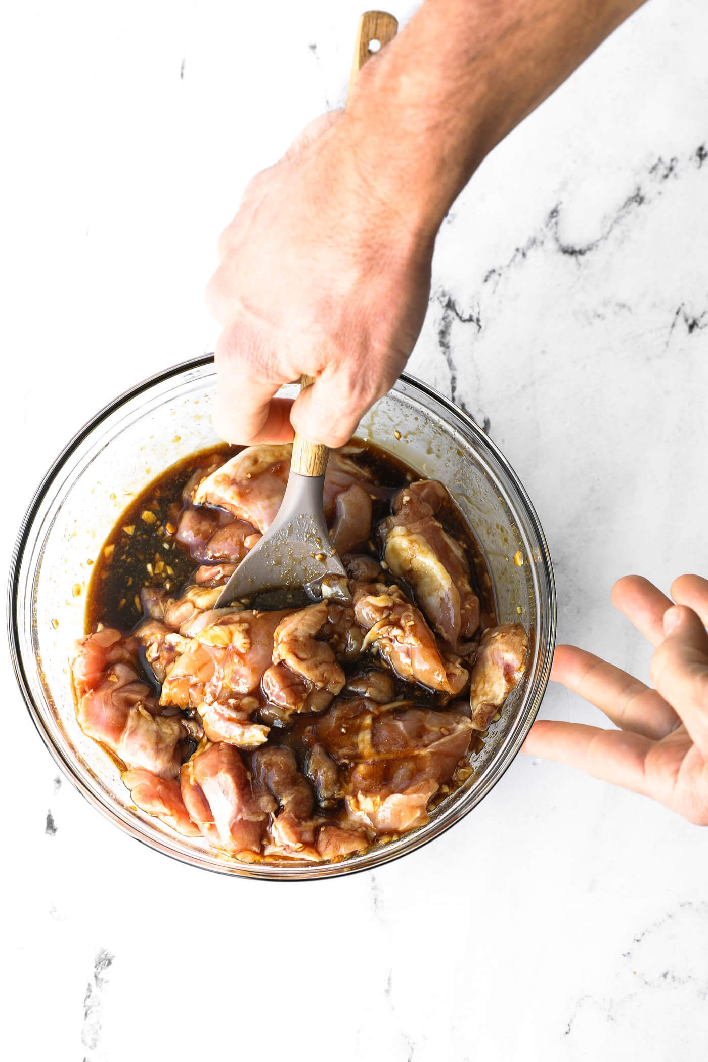 Mixing raw chicken with the honey garlic marinade in a glass bowl.
