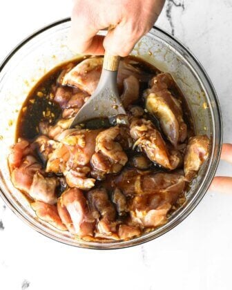 Stirring honey garlic marinade with raw chicken in a bowl.