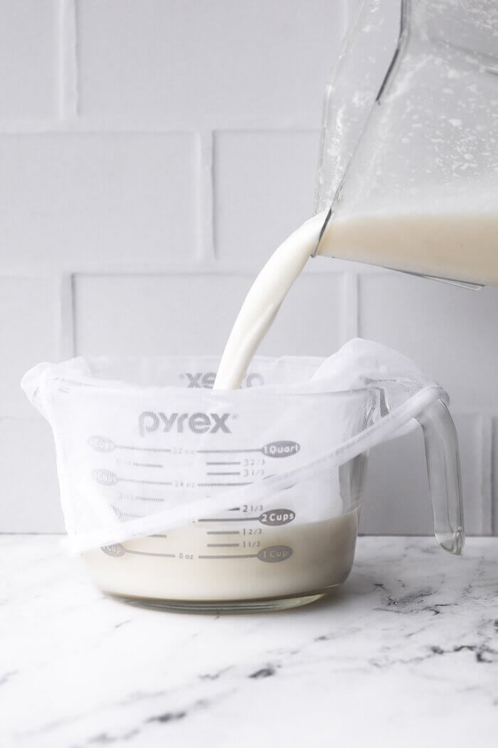 Pouring coconut milk in a jar with a nut milk bag for straining.