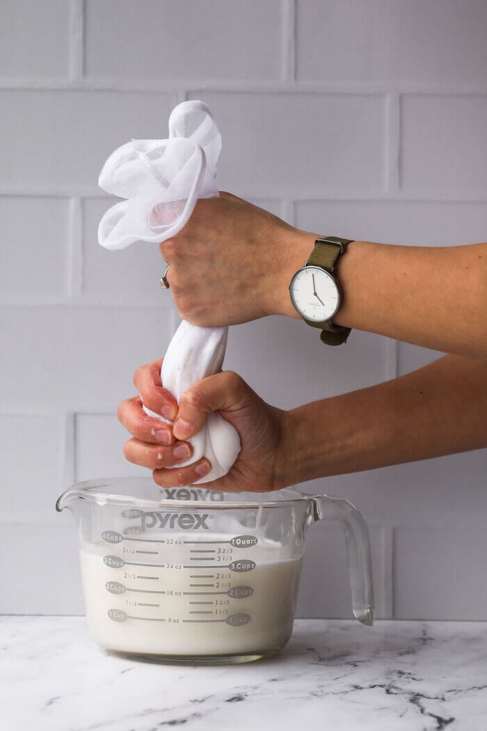 Squeezing out a nut milk bag over a jar after blending coconut milk to strain the milk.