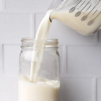 Pouring strained coconut milk into a mason jar for storing in the fridge.