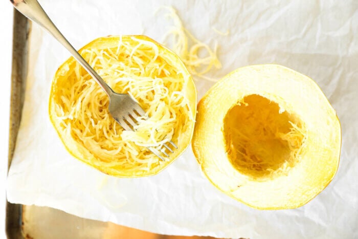 Roasted spaghetti squash on a baking sheet with the noodles scooped out in one half.